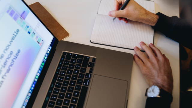 une personne qui eฬcrit sur un carnet, un ordinateur sur la table